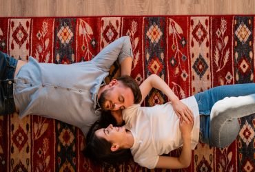 Top view young charming couple looking to each other smiling while lying on a colorful carpet with folk ornaments